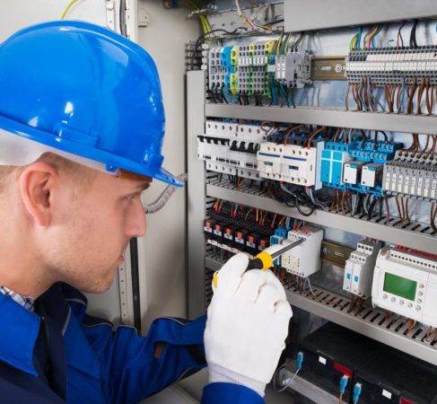 Male Electrician Working On Fusebox With Screwdriver